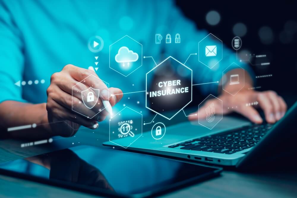 Laptop aperto con due mani in primo piano che interagiscono con una grafica che ha come tema l'assicurazione informatica.